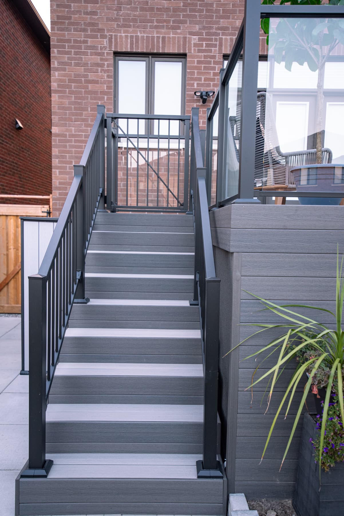 Grey composite deck stairs with black aluminum railing and glass deck guard